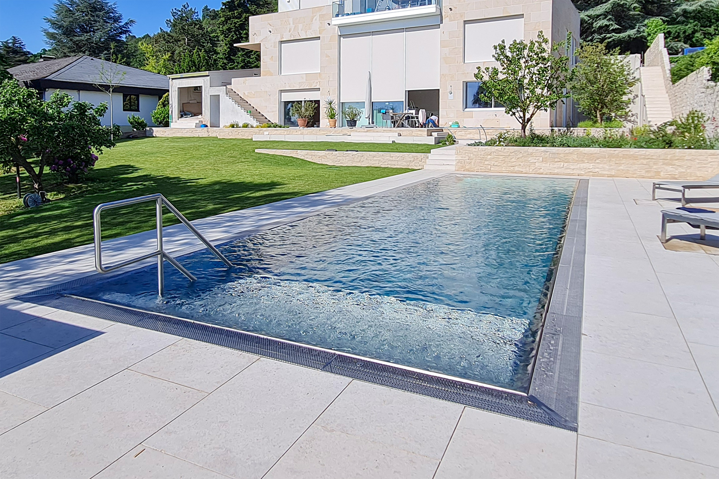 Edelstahlpool mit aktiver Wasserbewegung an der Luftsprudelliege, eingebettet in eine gepflegte Rasen- und Gartenanlage