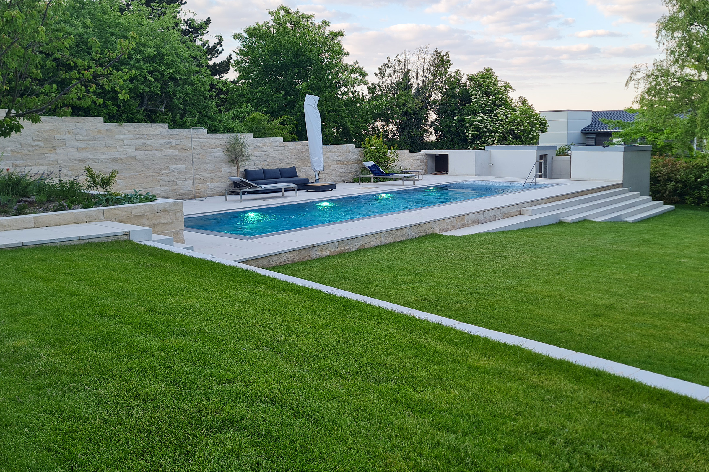 Edelstahlpool mit eingeschalteter LED-Beleuchtung bei Dämmerung, eingebettet in modern gestaltete Gartenanlage