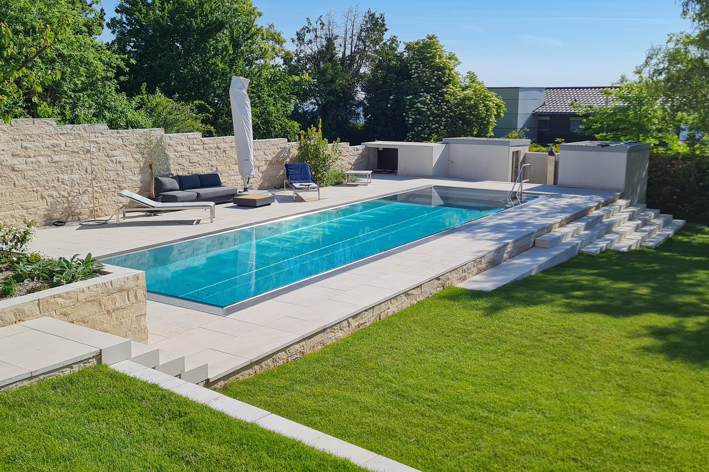 Edelstahlpool mit flacher Unterflurabdeckung aus Polycarbonatlamellen und modernem Außenbereich