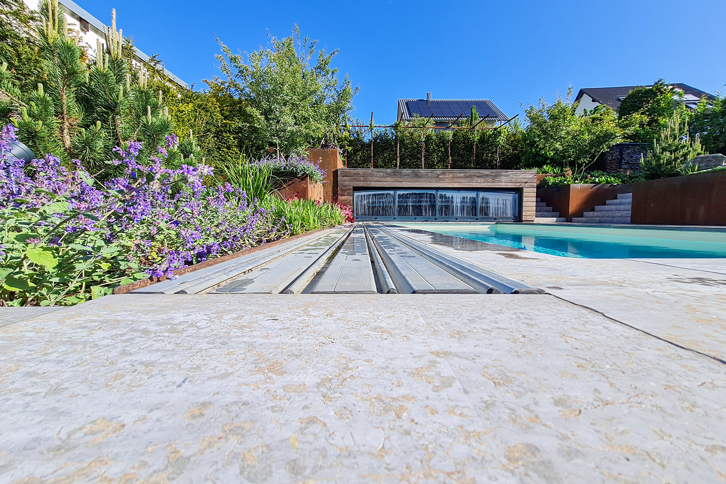 Detailansicht der flachen Laufschiene einer Poolüberdachung mit umgebender Bepflanzung